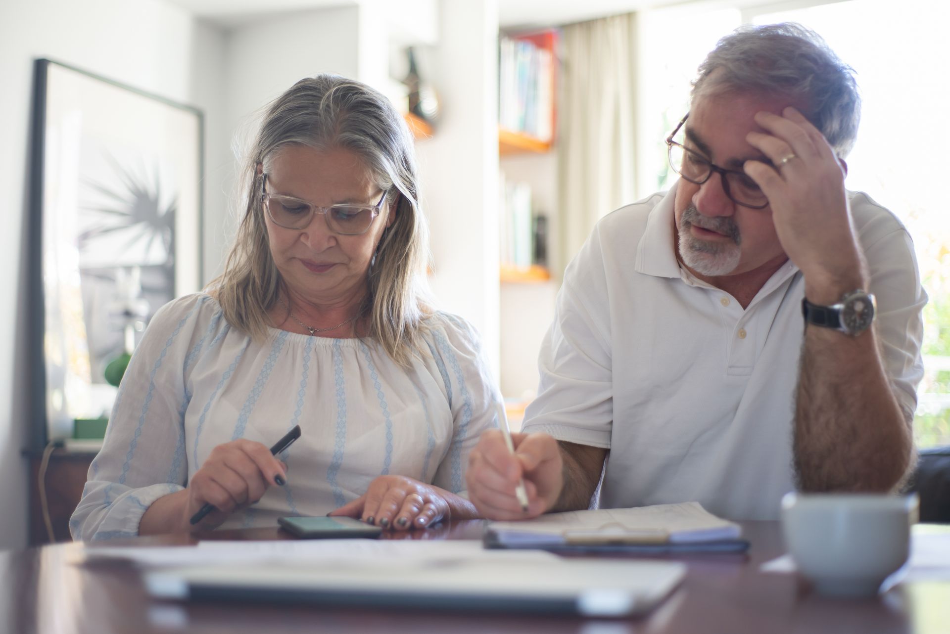 A retired couple reviewing paperwork together at a table at home while checking their benefit figures